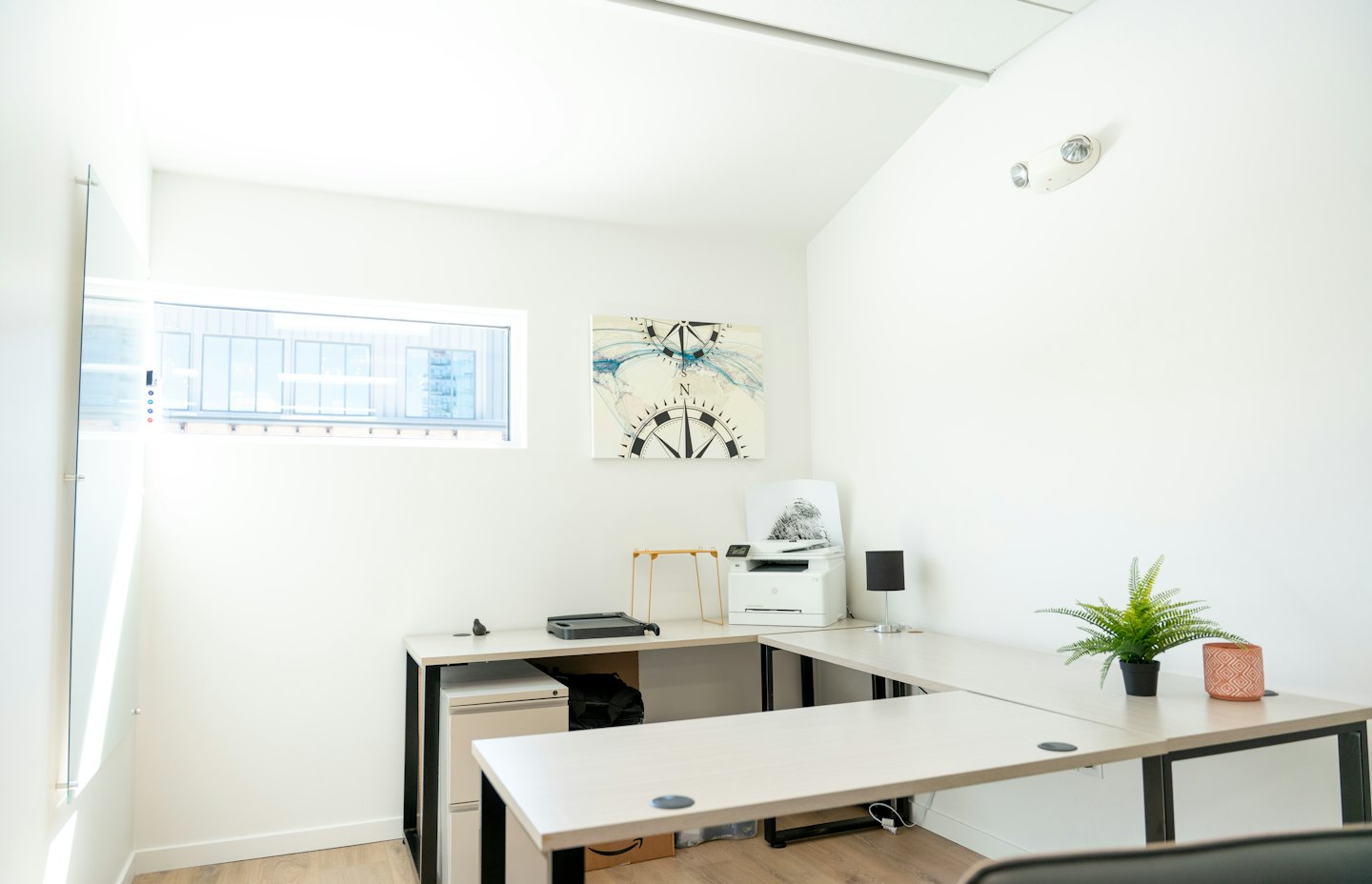 Ufficio domestico minimalista con scrivania a L e opera d'arte a forma di bussola.
